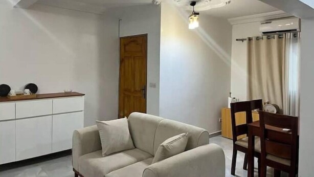Ein modernes Wohnzimmer mit einer Couch, einem Esstisch mit Stühlen, einer Holztür und einer Deckenleuchte.