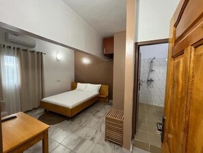 Una habitación pequeña y limpia con cama, escritorio y zona de ducha.