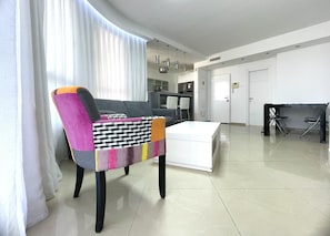A modern living room with a sofa, a coffee table, and a dining area with chairs and a table. - LOVELY 2BR GOLF RESIDENCE EILAT (Eilat)