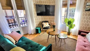 A living room with a teal sofa, a pink sofa, a wooden coffee table, and a TV mounted on the wall.