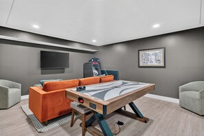 A modern living room with a pool table, a sofa, a gaming chair, a flat-screen TV, and a framed picture on the wall.