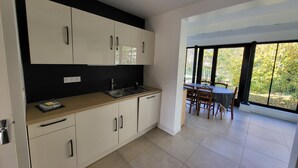 A modern kitchen with white cabinets and a black backsplash, leading to a dining area with a table and chairs. - Createur DE Souvenirs (Chartres)