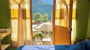 Un dormitorio con una cama grande, techo de madera y vista a un paisaje montañoso a través de una puerta abierta.
