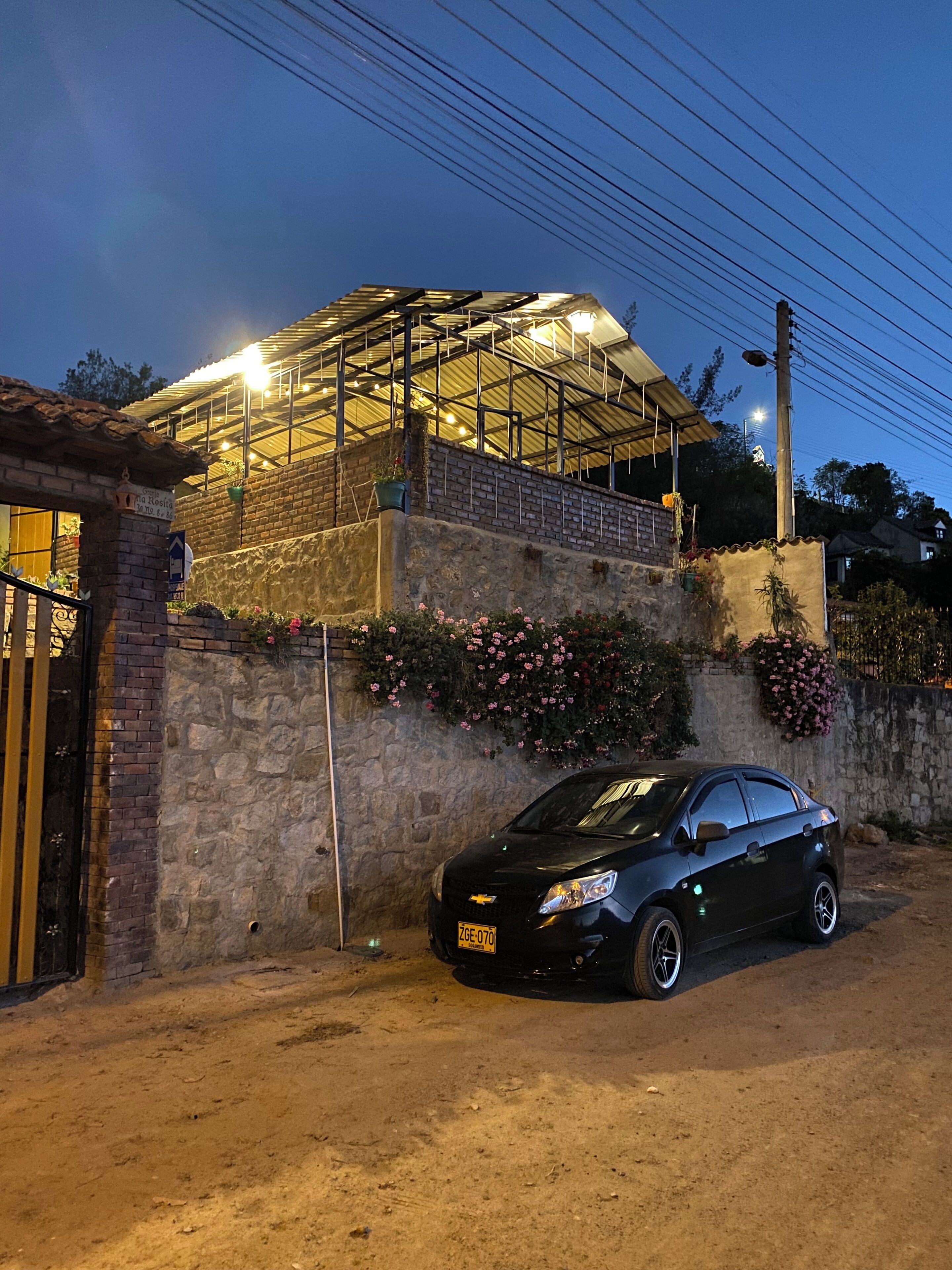 A black car parked in front of a building with a brick wall and a metal roof structure.