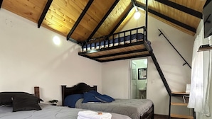 Un dormitorio con dos camas, suelo de madera, techo inclinado con vigas a la vista y una ventana pequeña.