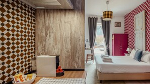 Una habitación con pared estampada, panel de madera, cama con colchón blanco, armario rojo y un área de comedor con mesa y sillas.