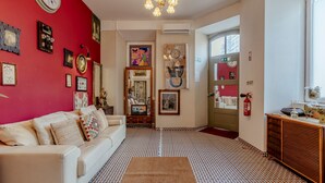 Una sala de estar con una pared roja, un sofá blanco y un suelo estampado. Hay cuadros enmarcados y un reloj en la pared.