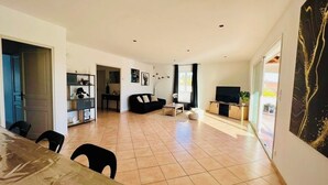 Ein geräumiger Wohnbereich mit Esstisch, schwarzen Sofas, einem Fernseher und Kunstwerken an den Wänden.