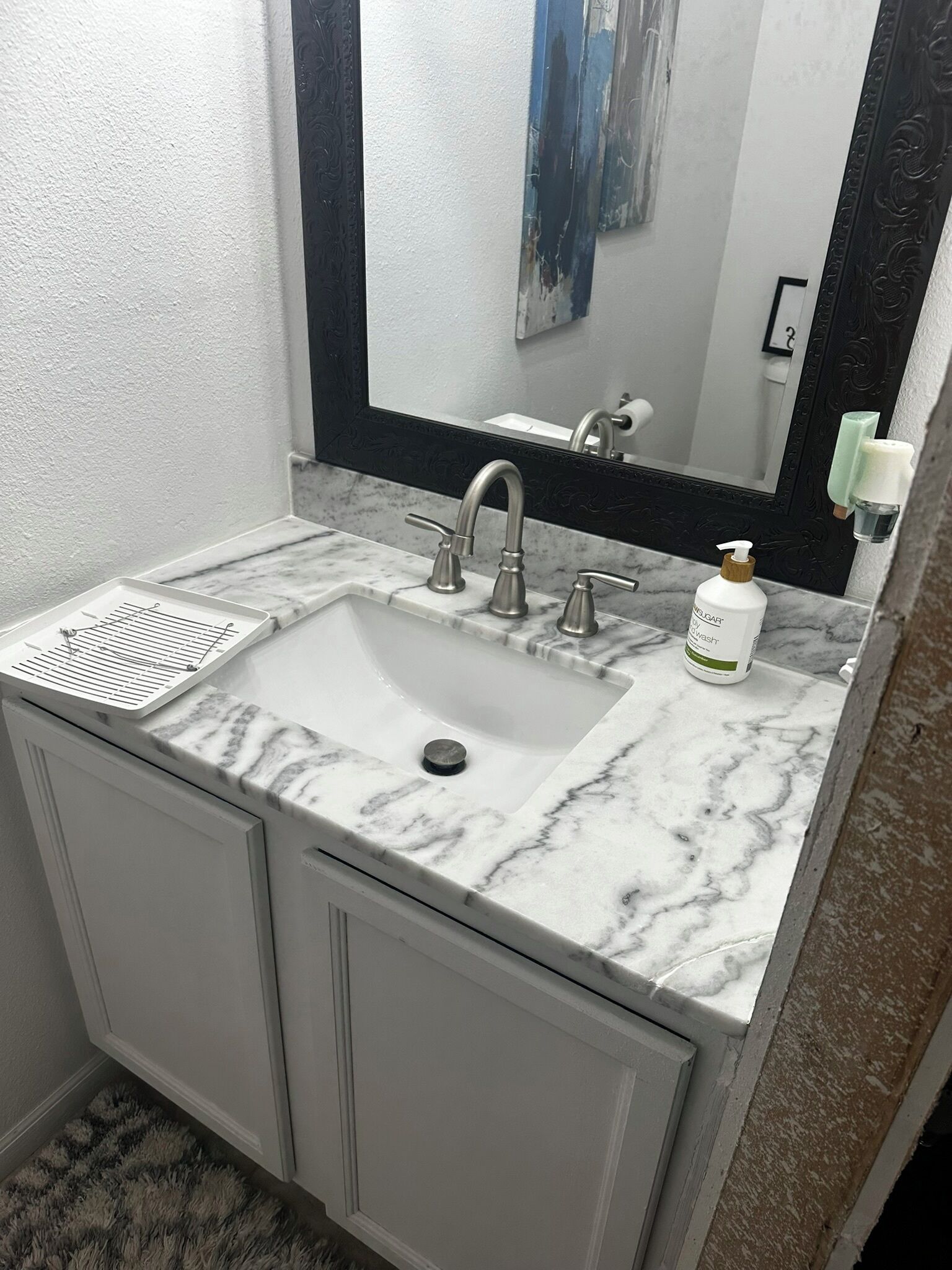 Un baño con lavabo de mármol, dos grifos, un espejo y dispensador de jabón.