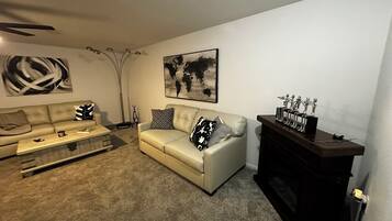 A living room with a beige sofa, a glass coffee table, a dark wooden cabinet, and a large abstract painting on the wall.