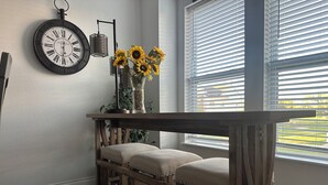 A dining area with a wooden table and chairs, a wall clock, and a window with blinds. - Capital City- 6 Miles from Madison with fireplace (Sun Prairie)