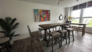 A modern kitchen with a wooden table and bar stools, a large abstract painting on the wall, and a potted plant. - Capital City- 6 Miles from Madison with fireplace (Sun Prairie)