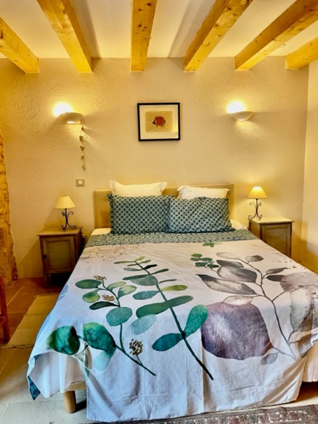 Un dormitorio con cama, dos mesitas de noche, un cuadro en la pared y vigas de madera en el techo.