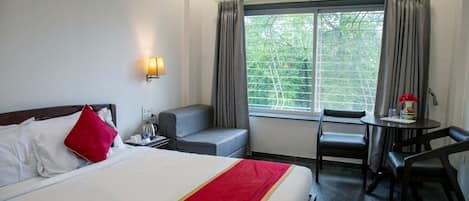 Une chambre d’hôtel avec un lit, un bureau, une chaise, une table et une fenêtre avec des rideaux.
