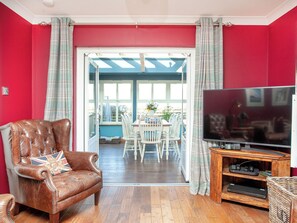 A living room with a leather armchair, a television, and a dining area with a table and chairs.