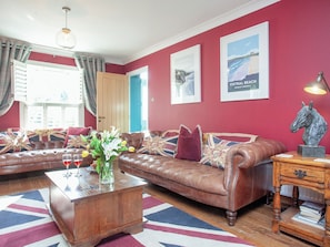 A living room with a brown leather sofa, a wooden coffee table, and a red wall with two framed pictures.