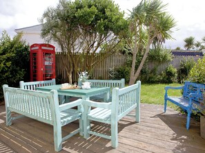 A wooden deck with a table and chairs, a red telephone booth, and a blue bench. - 4 bedroom accommodation in Newquay (Newquay)