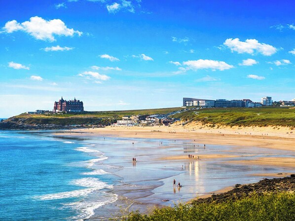 A coastal beach with a castle and modern buildings in the background.
