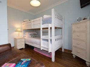 Un lit superposé avec une table de chevet, une commode et un canapé en cuir marron dans une pièce dont le sol est recouvert de parquet.