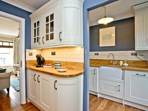 Una cocina con armarios blancos, encimera de madera y una lámpara colgante.