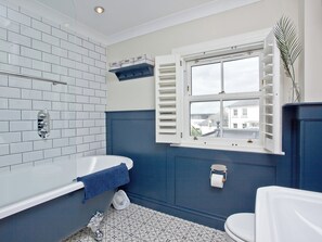A bathroom with a bathtub, toilet, and window with shutters. - 4 bedroom accommodation in Newquay (Newquay)