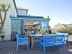 A coastal house with a blue exterior, a wooden deck, and a dining area with blue furniture.