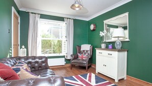 Una stanza con una parete verde, un termosifone bianco, un divano in pelle marrone, un armadietto bianco e un tappeto con la Union Jack.
