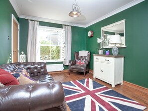 Una habitación con pared verde, radiador blanco, sofá de cuero marrón, mueble blanco y alfombra con motivo de la bandera del Reino Unido.