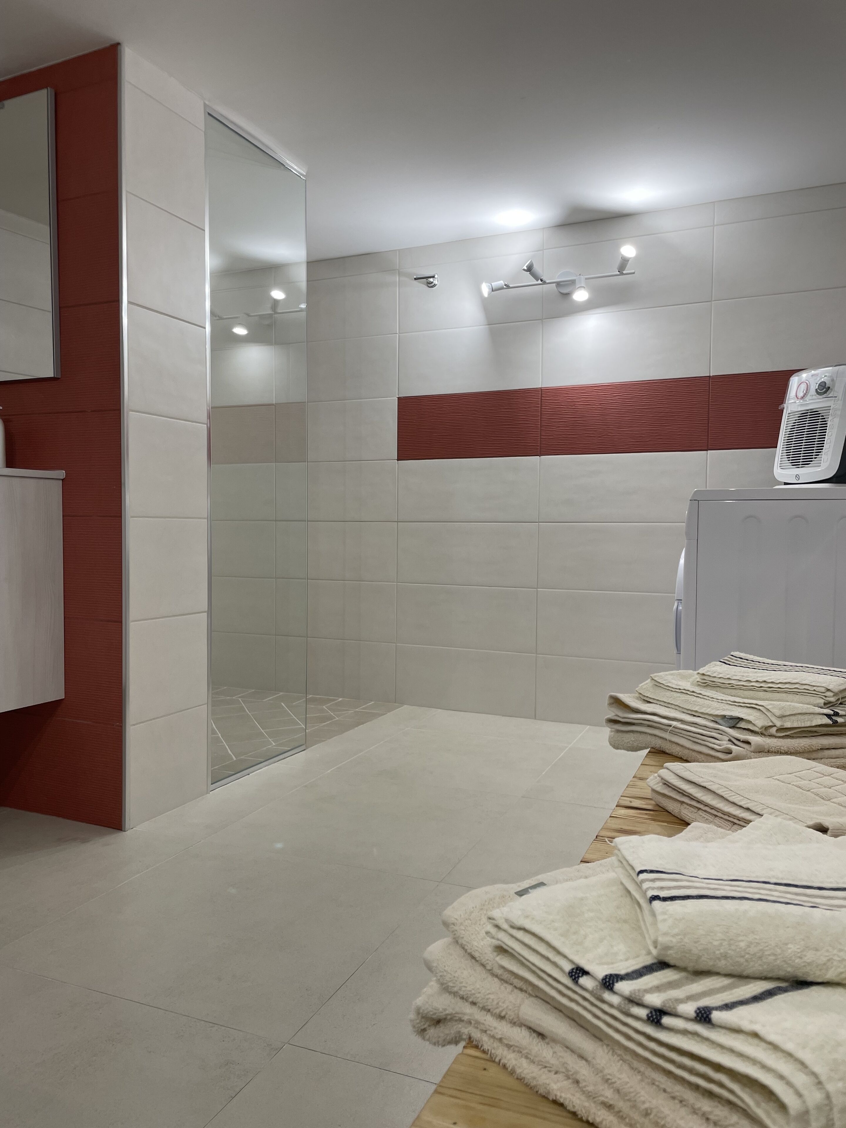 A modern bathroom with a glass shower enclosure, a white towel rack, and a stack of folded towels on a wooden table.