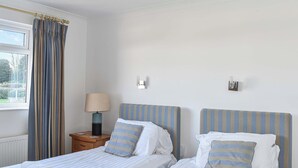 Habitación de hotel con dos camas individuales, una mesita de noche con lámpara, una ventana con cortinas y vistas al exterior.