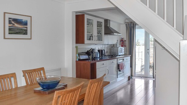 Una cocina moderna con armarios blancos, una mesa de comedor de madera y vistas al exterior.
