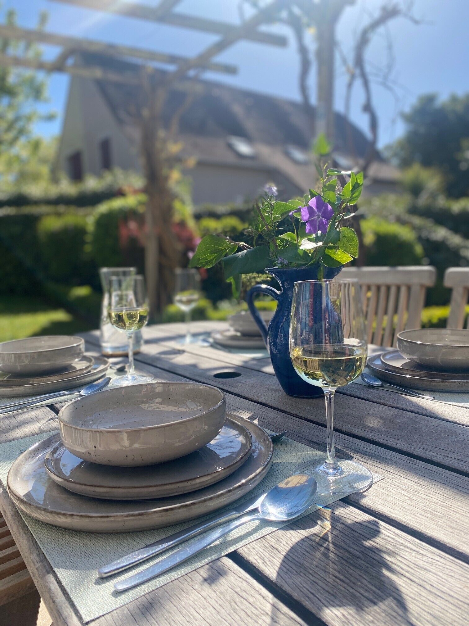 A wooden table set for dining with plates, cutlery, and a glass of white wine.