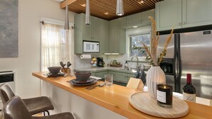 A modern kitchen with a wooden countertop, stainless steel appliances, and a large window. - The Hattie House in Old Town – Walk Everywhere! (Fort Collins)