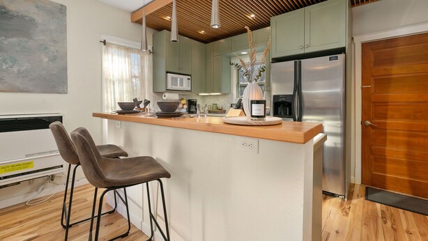 A modern kitchen with a wooden countertop, two bar stools, a stainless steel refrigerator, and a microwave. - The Hattie House in Old Town – Walk Everywhere! (Fort Collins)