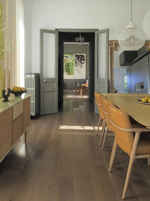 A modern kitchen with wooden flooring, a dining area with yellow chairs, and a view of the outdoors through an open door. - Maison de Charme vue mer Avec Piscine au Centre de Marseille (Marseille)