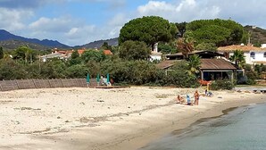 A beach with clear water, a few people, and buildings in the background.