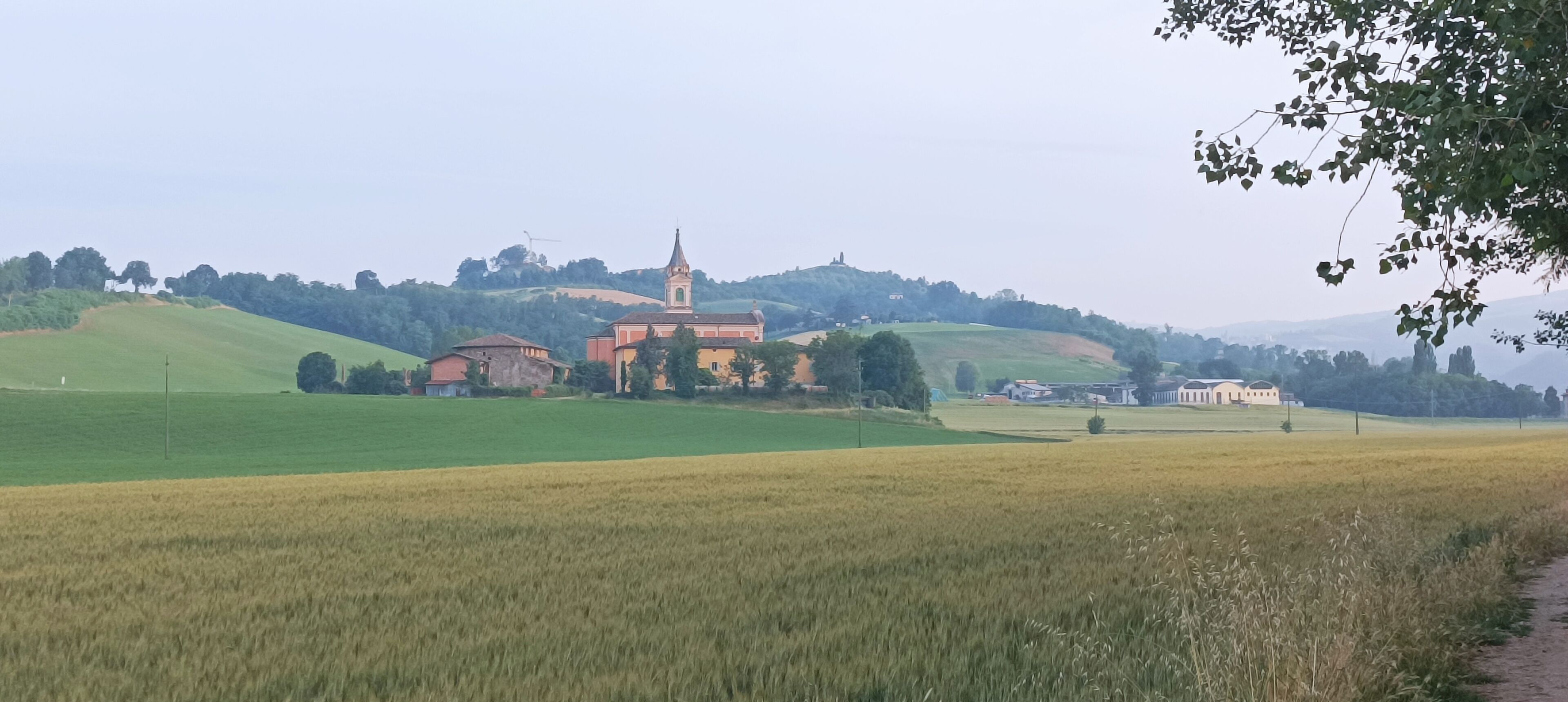 Paisagem rural com uma igreja, campos e uma colina ao fundo.