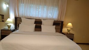 A neatly made bed with white linens, two bedside lamps, and a window with sheer curtains.