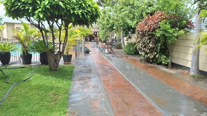A paved pathway flanked by potted plants and a thatched-roof structure.