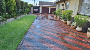 A paved pathway with a mix of red and black bricks, flanked by green grass and potted plants.