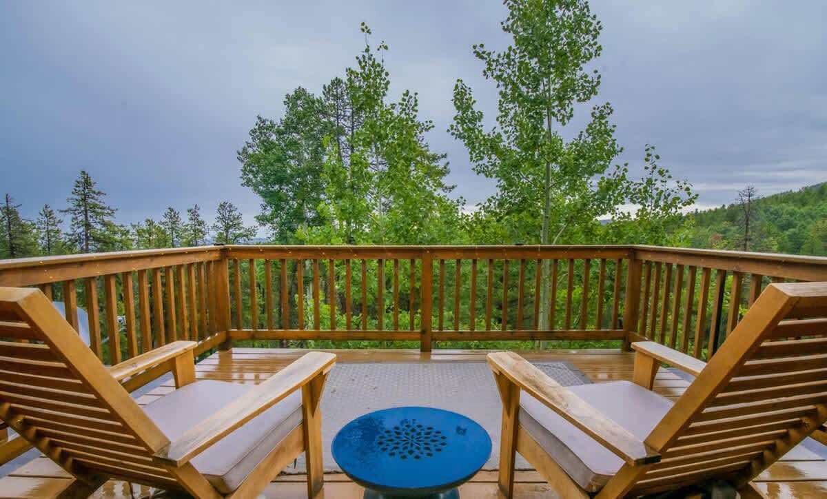 Ett trädäck med två solstolar och ett litet bord, omgivet av ett räcke, med utsikt över ett skogsområde.
