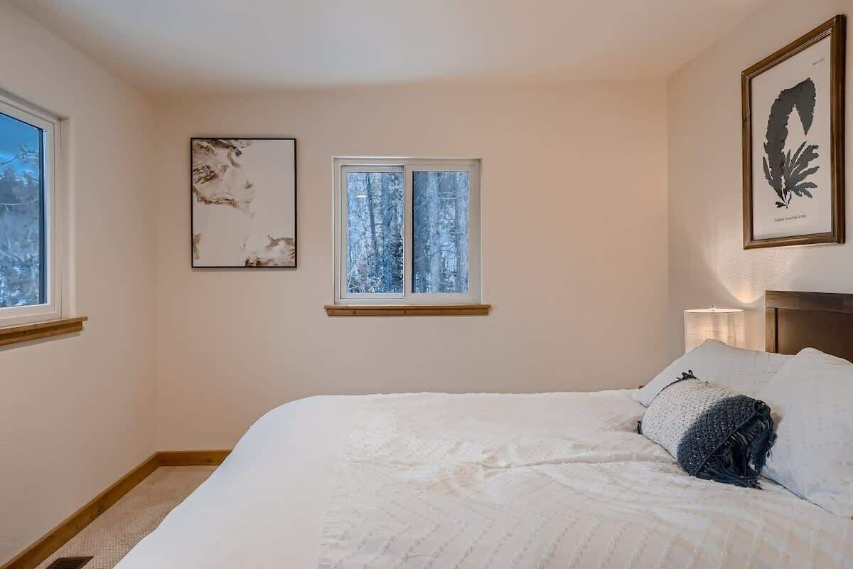 A bedroom with a large bed, a window with a view of snow-covered trees, and two framed artworks on the walls.