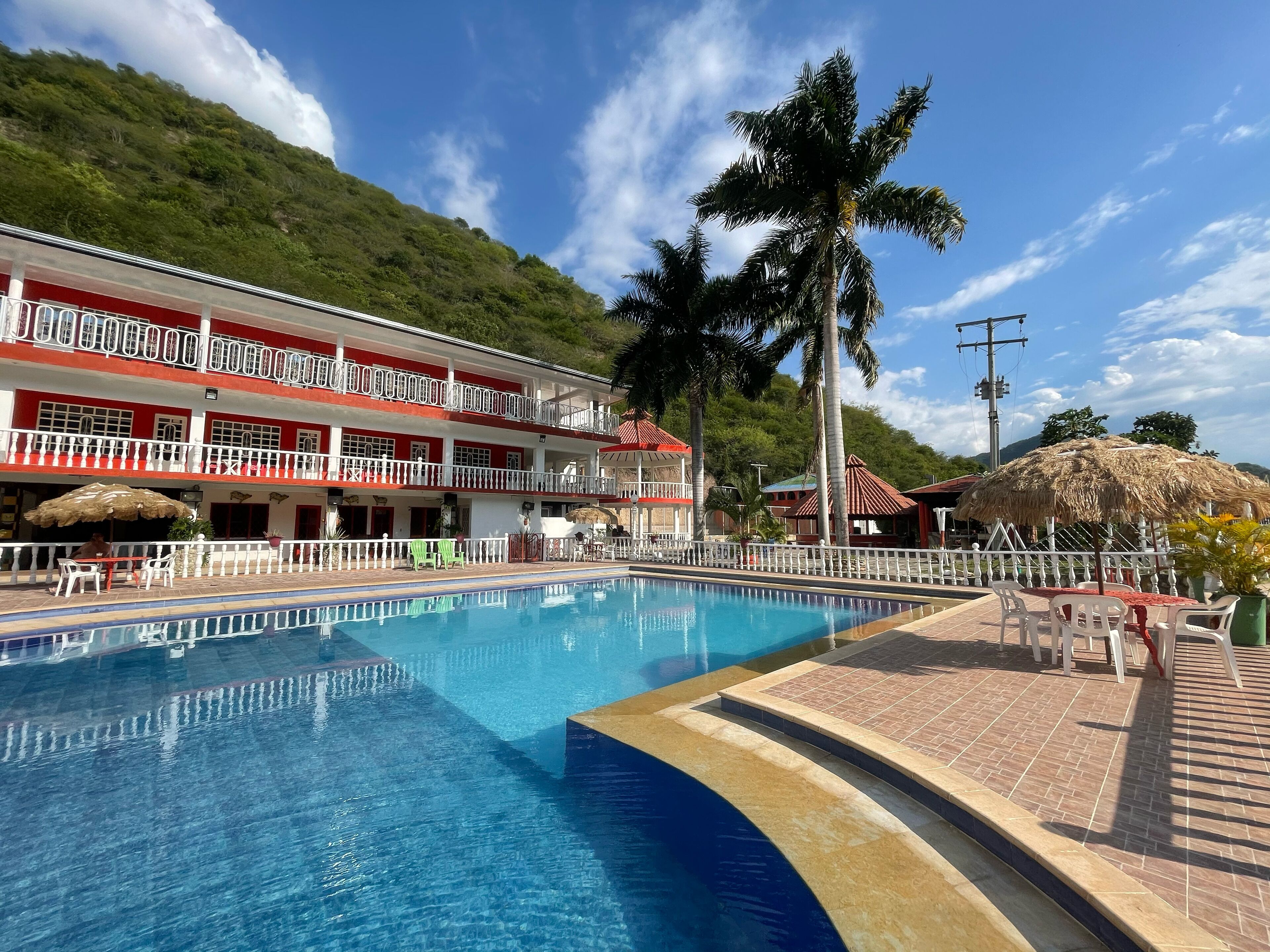 Ein Hotel mit Schwimmbad, Außenbereich und einem rot-weißen Gebäude mit Balkonen.