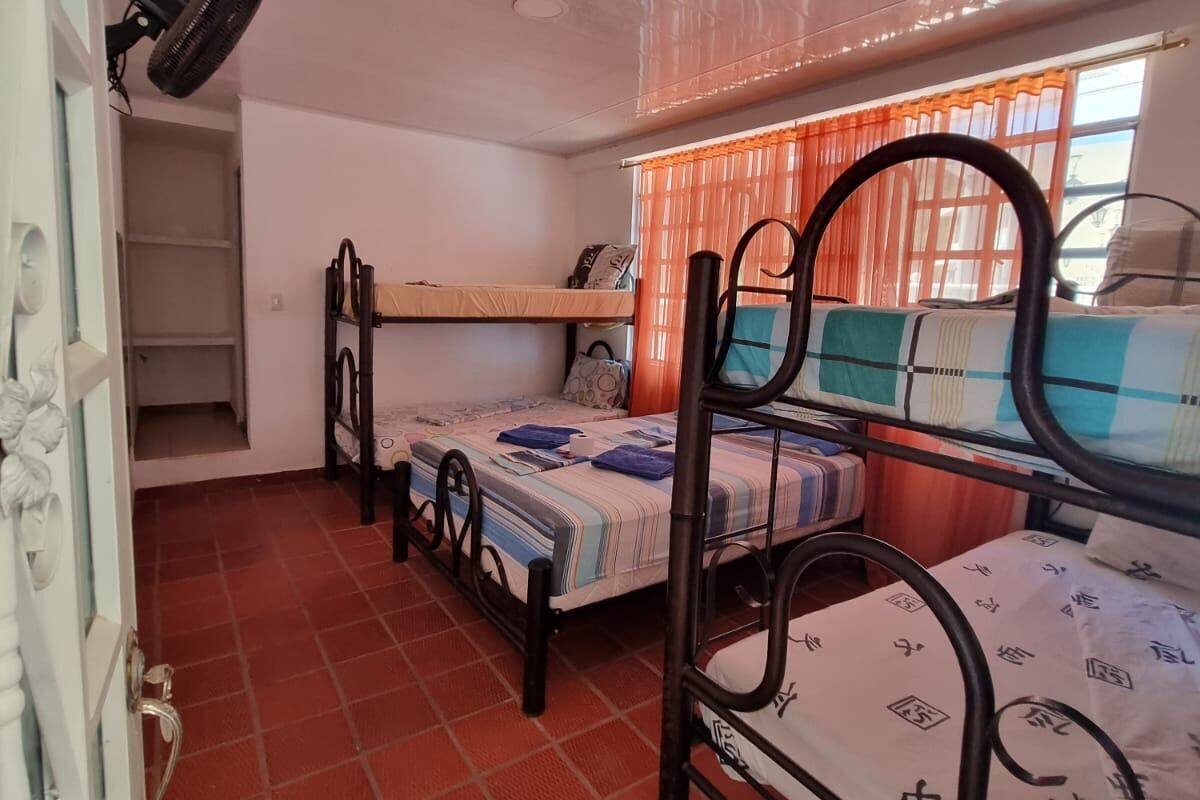 A dormitory room with bunk beds, a fan, a window with orange curtains, and a door with a decorative handle.
