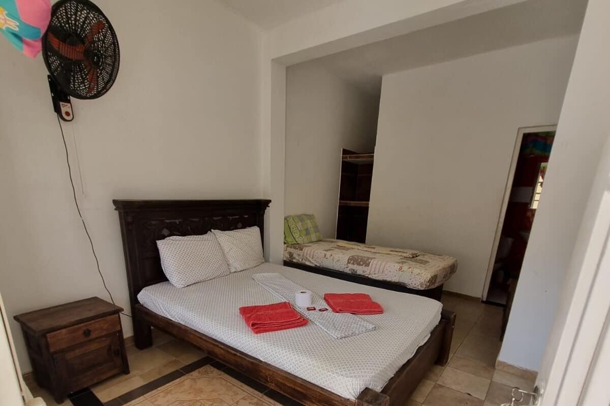 A bedroom with a wooden bed, a nightstand, a fan, and a tiled floor.