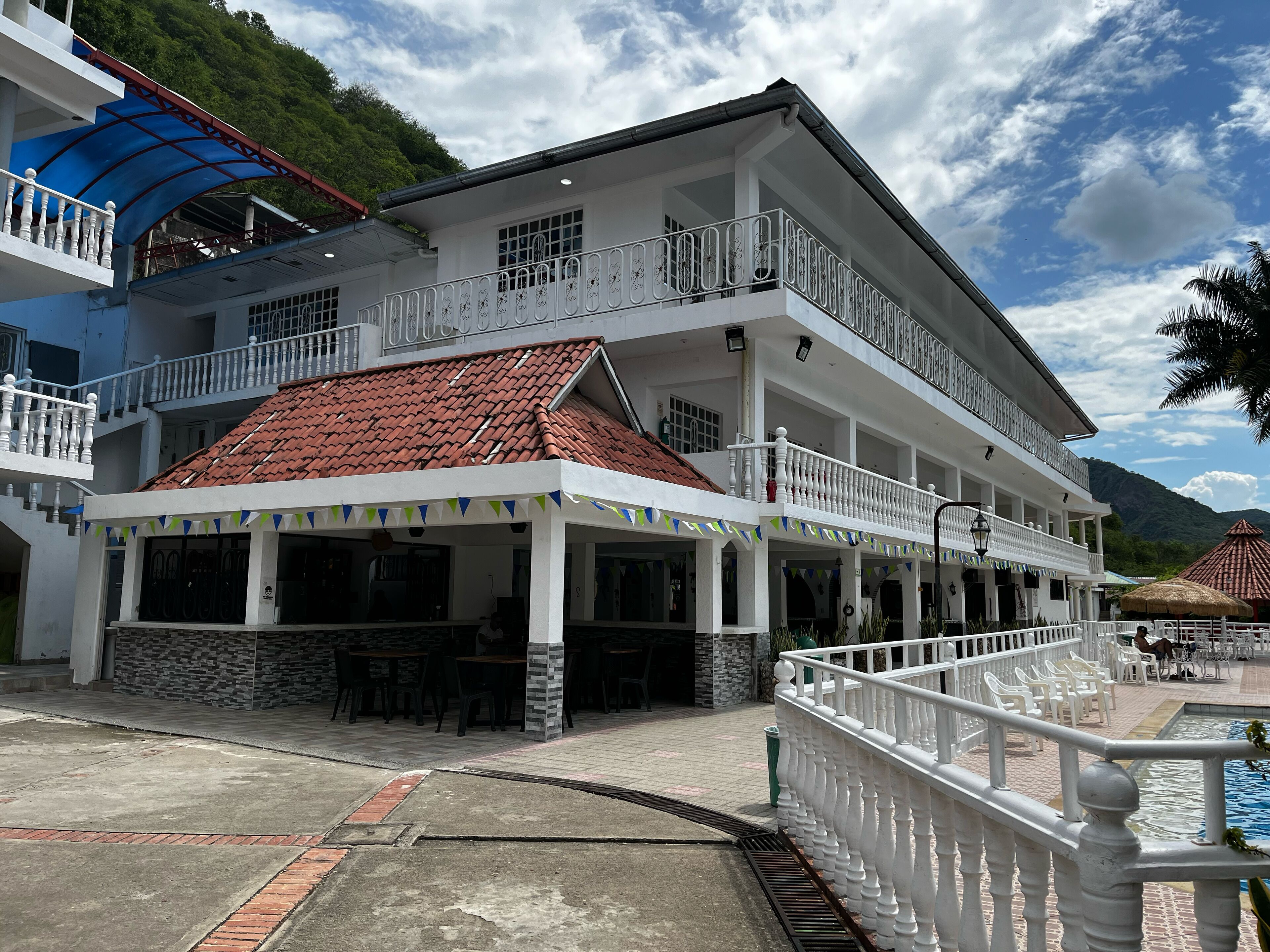 A two-story building with a red-tiled roof, white balconies, and a covered outdoor seating area.