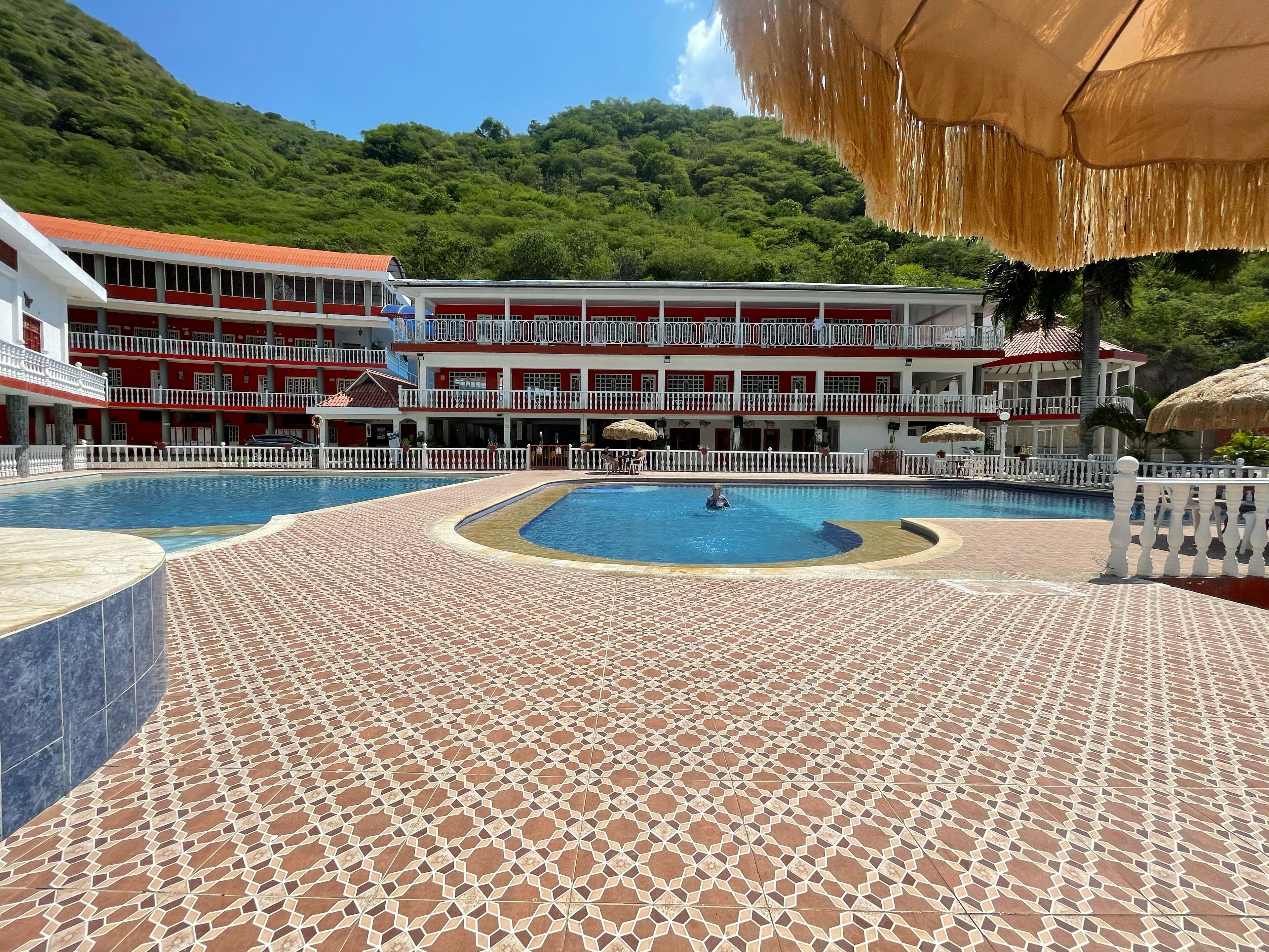 A hotel with a pool area, a red and white building, and a mountainous backdrop.