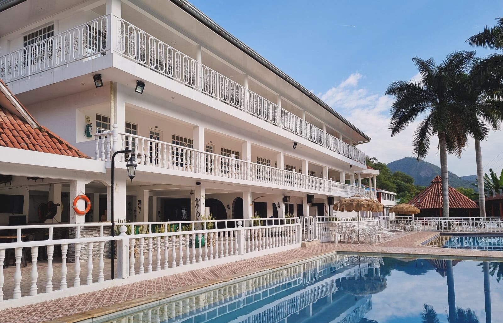 Un hotel de varios pisos con piscina, balcones y montañas al fondo.