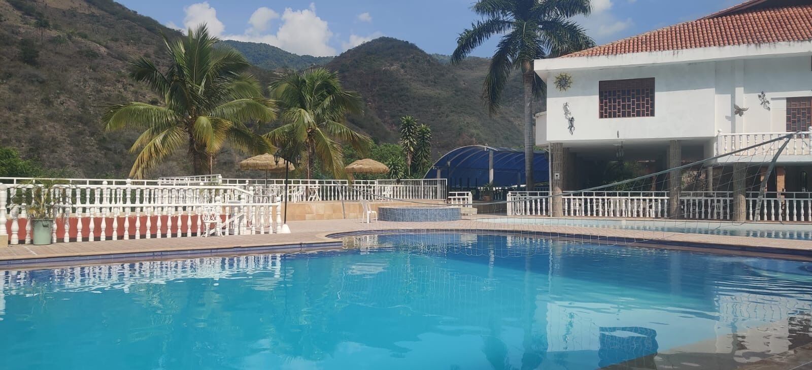 Una piscina con valla blanca, palmeras y un edificio con techo rojo.
