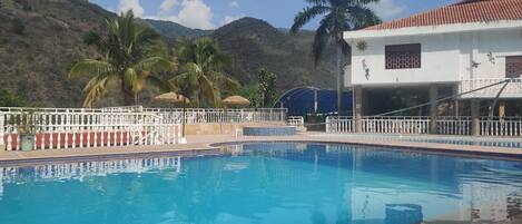 Una piscina con valla blanca, palmeras y un edificio con techo rojo.